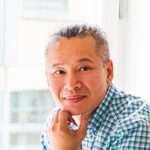 Homme avec une chemise à carreaux, posant avec un léger sourire et une main sous le menton.