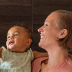 Femme souriante tenant un bébé dans ses bras, tous deux regardant vers le haut.