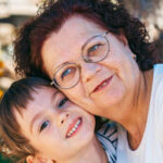 Femme avec des lunettes et un enfant souriant, posant ensemble pour une photo.