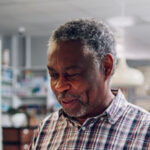 Homme d'âge moyen avec des cheveux gris et une chemise à carreaux, souriant légèrement.